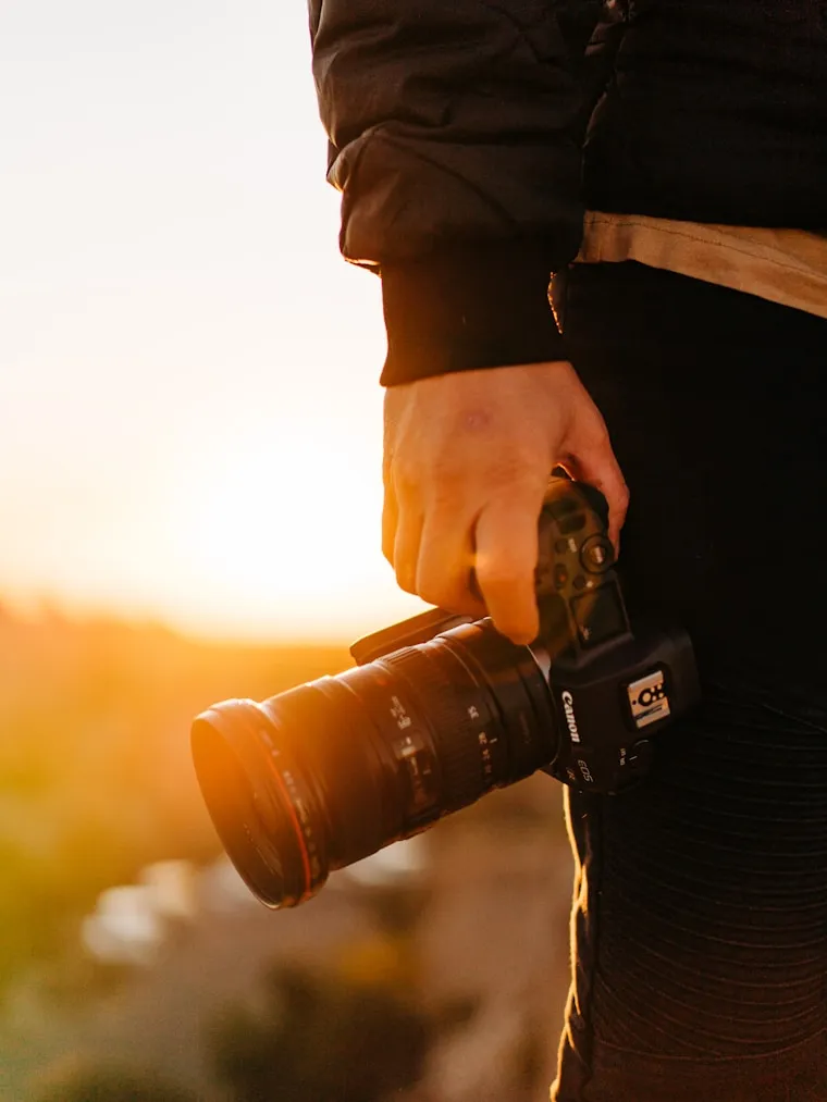 A hand holding a camera against a setting sun