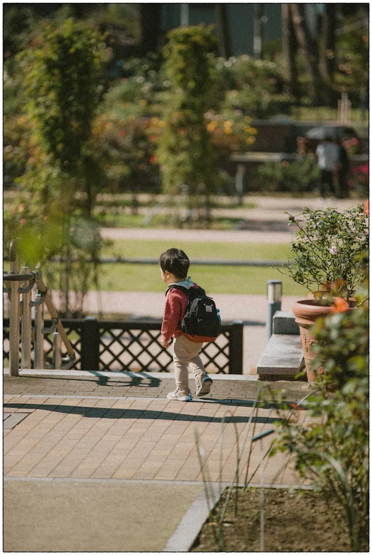 A boy with a backpack walking down a park path, from behind