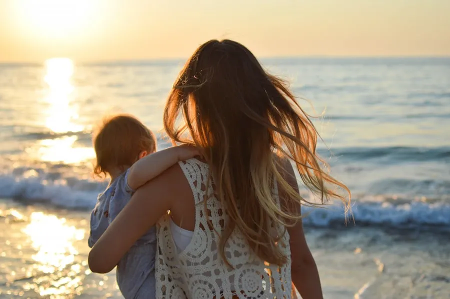 A mother holding a baby by a golden sea