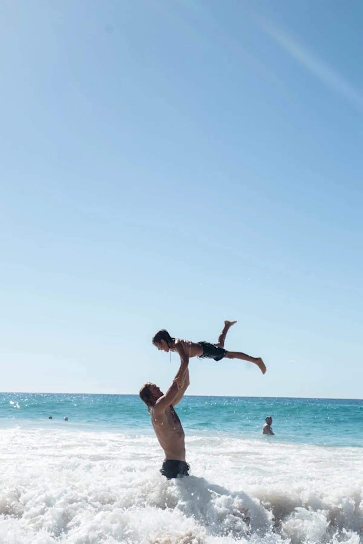 A dad tossing a kid over the waves